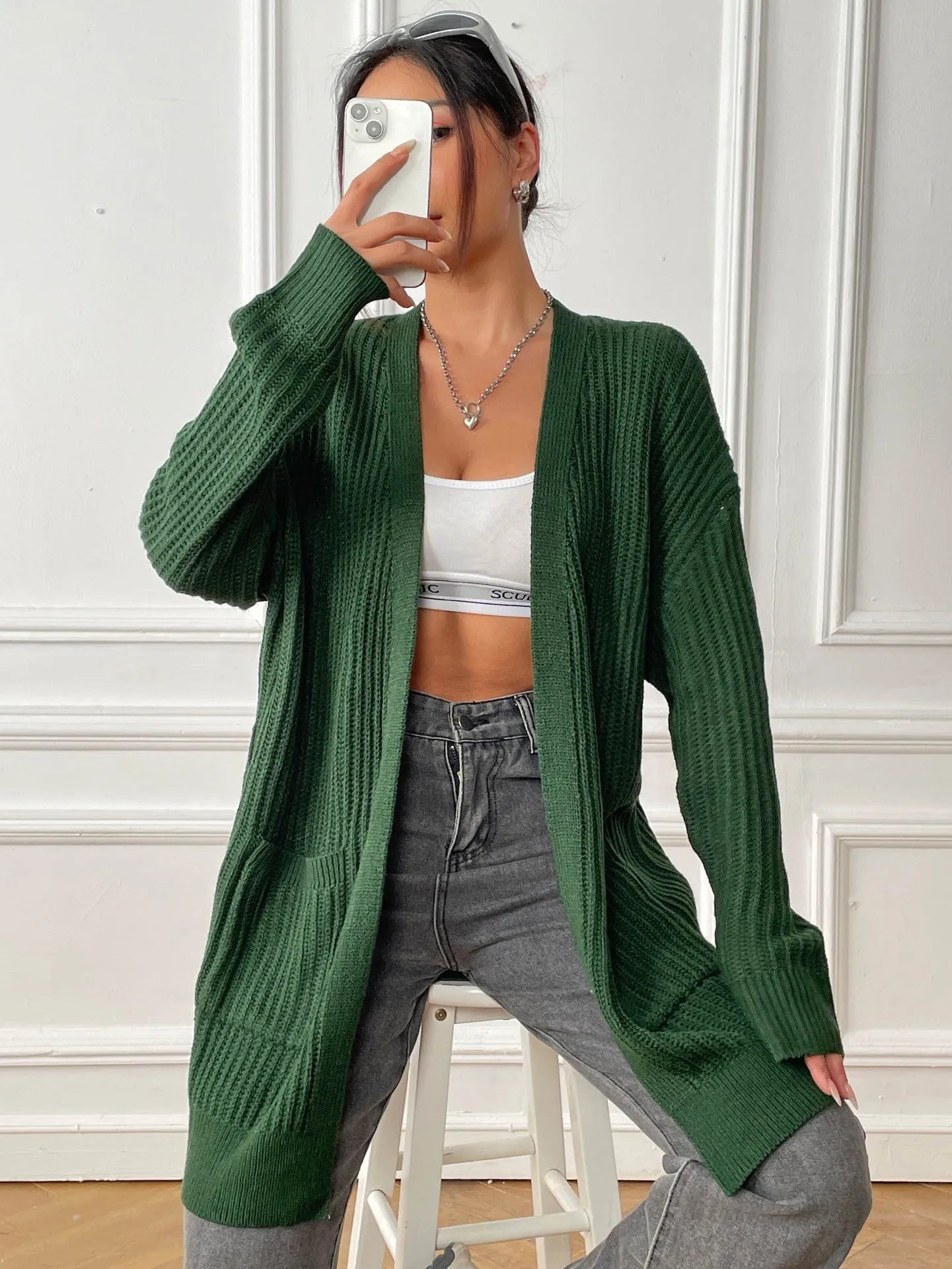 A loose-fitting, mid-length acrylic cardigan sweater in a solid colour, shown in a street hipster style.