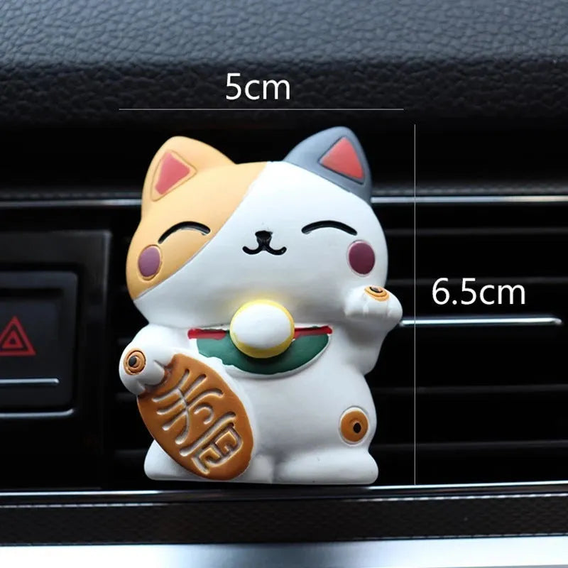 Black and white resin fortune cat ornament designed to clip onto a car air vent as an aromatherapy diffuser.