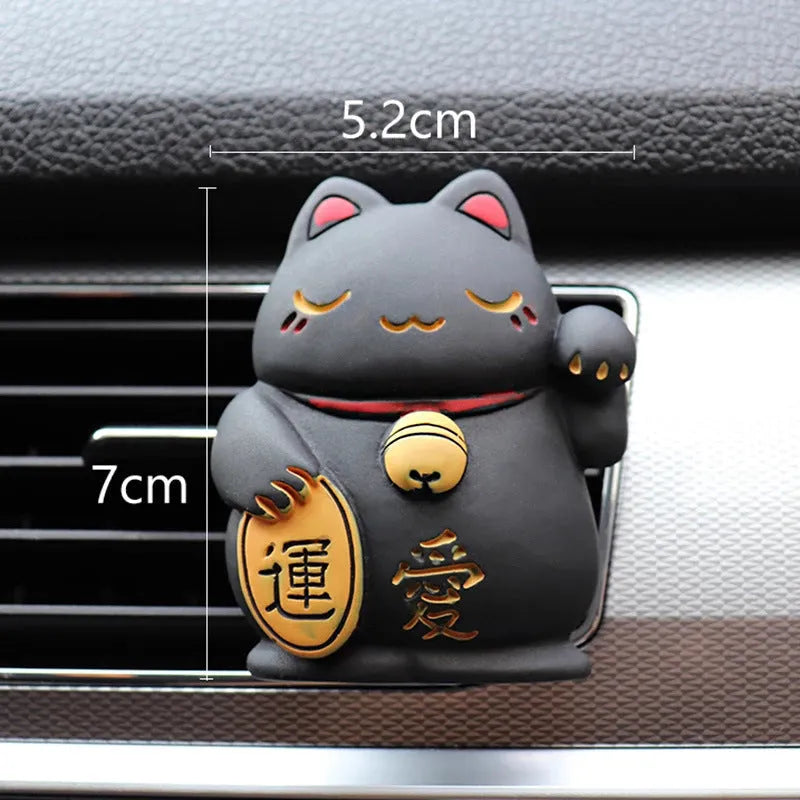 Black and white resin fortune cat ornament designed to clip onto a car air vent as an aromatherapy diffuser.