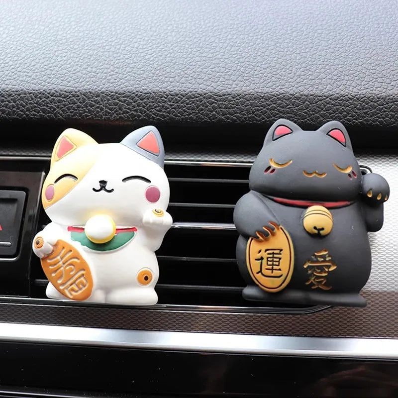 Black and white resin fortune cat ornament designed to clip onto a car air vent as an aromatherapy diffuser.