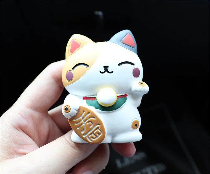 Black and white resin fortune cat ornament designed to clip onto a car air vent as an aromatherapy diffuser.