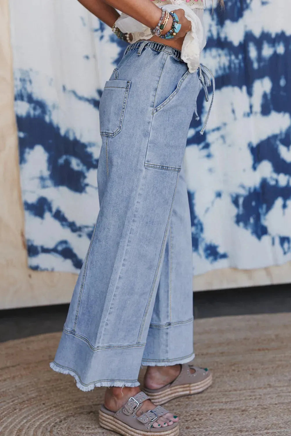 Beau blue wide leg denim trousers with a drawstring waist and raw hem detail laid flat.