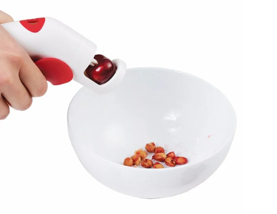 Red and black manual cherry pitter tool with detachable stone catcher on a kitchen worktop.