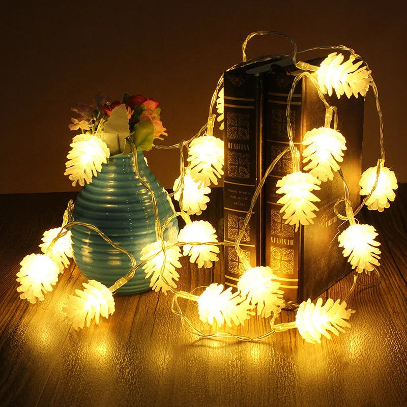 Warm white LED pine cone string lights draped over a surface, showing plastic shell details and battery pack.