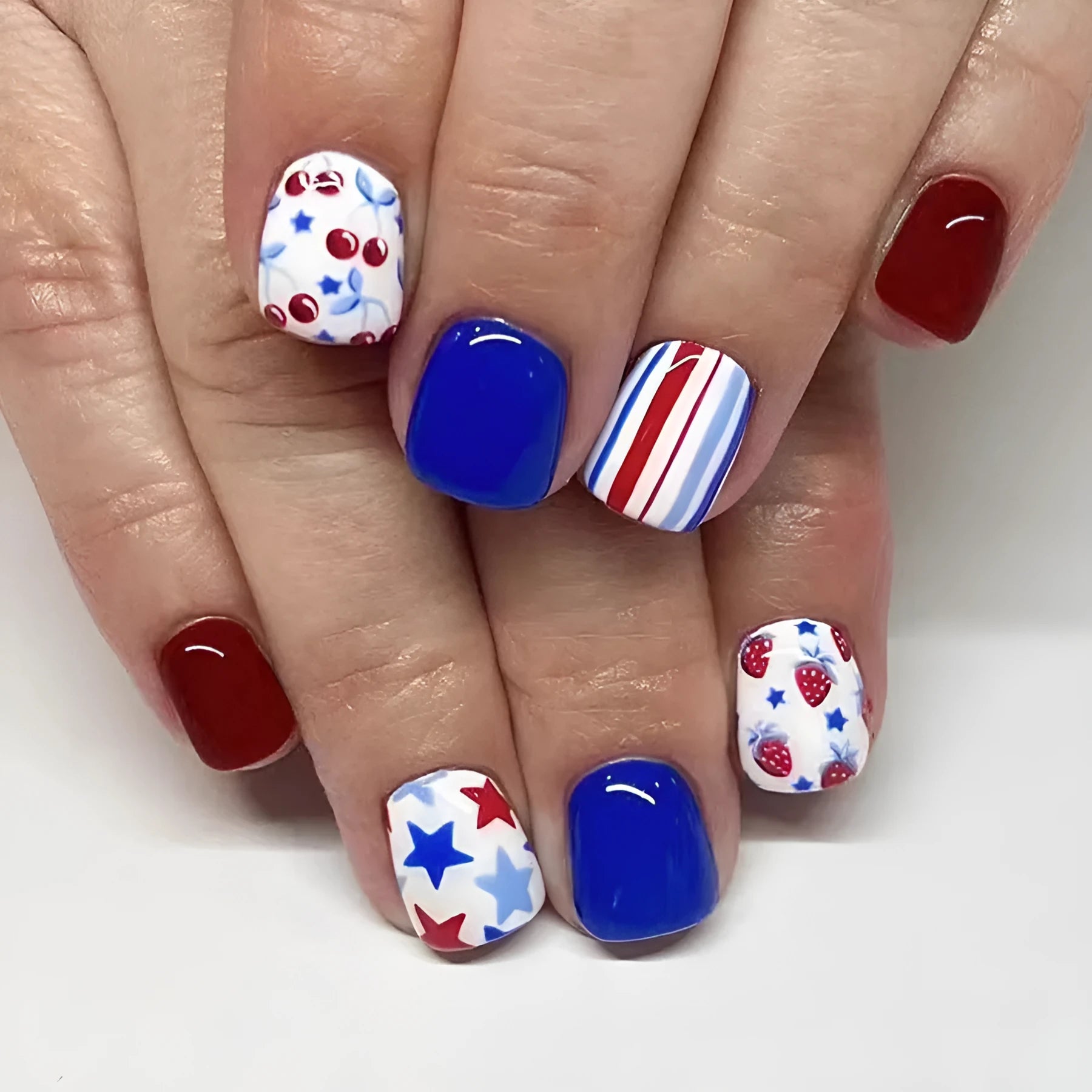 Short glossy false nails with strawberry and cherry patterns in red and blue colour combinations