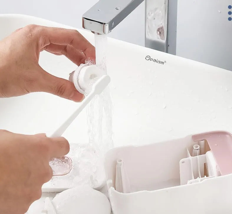 Wall-mounted automatic toothpaste dispenser in blue, grey, or pink colours with a visible dispensing lever.