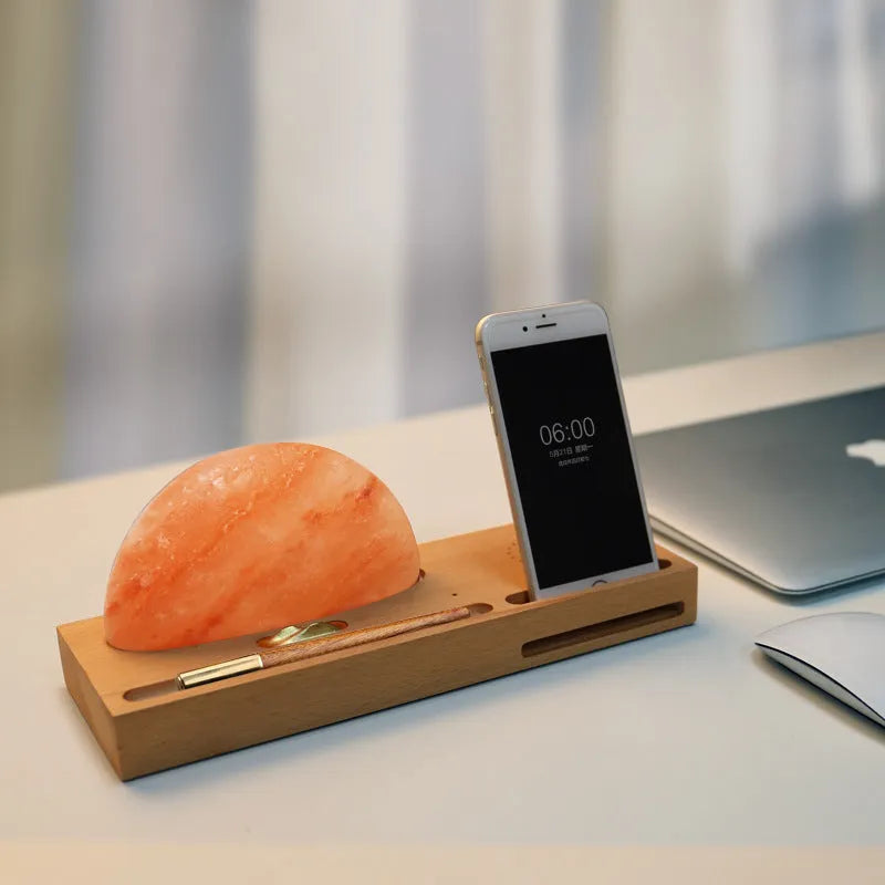 Wooden-based table lamp with a glowing orange Himalayan salt shade, wirelessly charging a mobile phone on its surface.