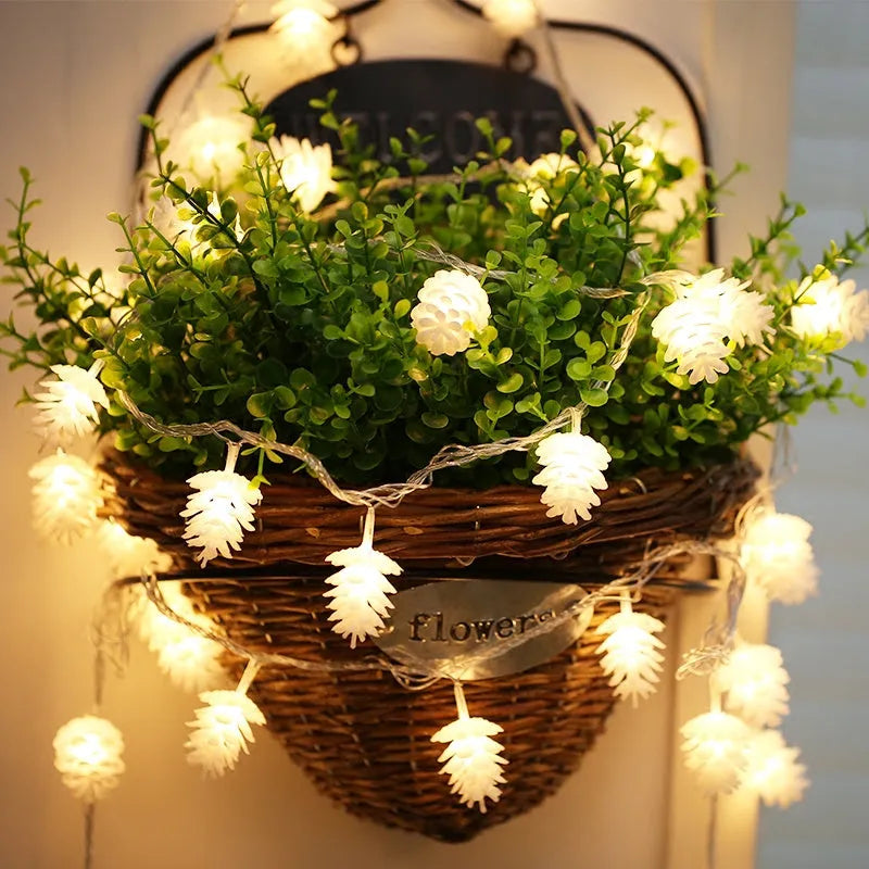 Warm white LED pine cone string lights draped over a surface, showing plastic shell details and battery pack.