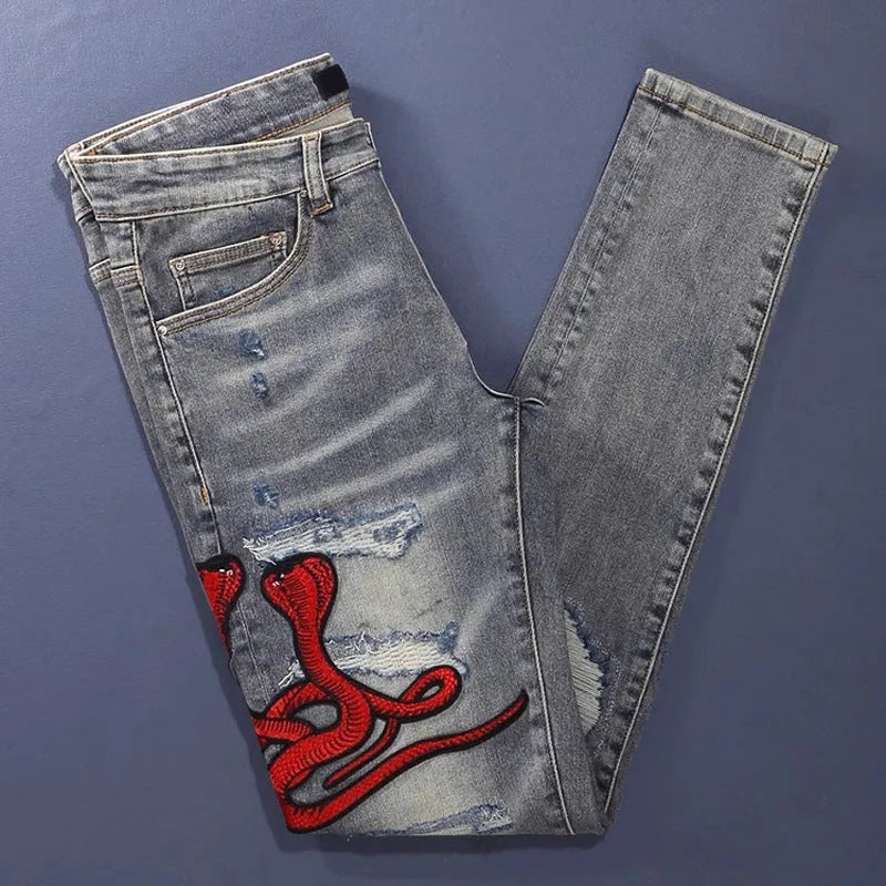 Close-up of distressed slim fit jeans showing worn wash, hole patches, and embroidery on blue denim.