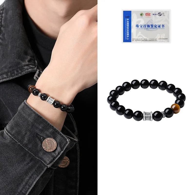 Men's black obsidian and silver bracelet with a 10mm prayer wheel charm on a dark background.