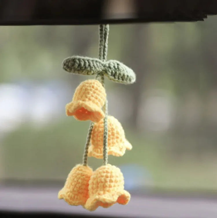 Green and white crocheted car plant decoration with hanging rope on a car dashboard.
