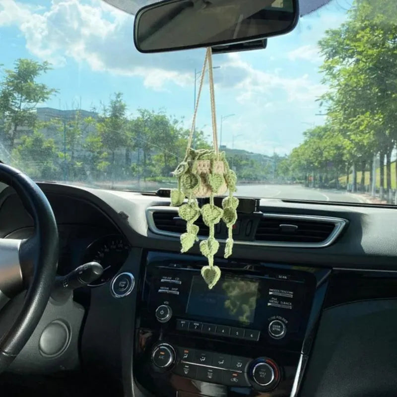 Green and white crocheted car plant decoration with hanging rope on a car dashboard.