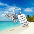 Stainless steel motorcycle key ring with velvet storage bag on a plain background.