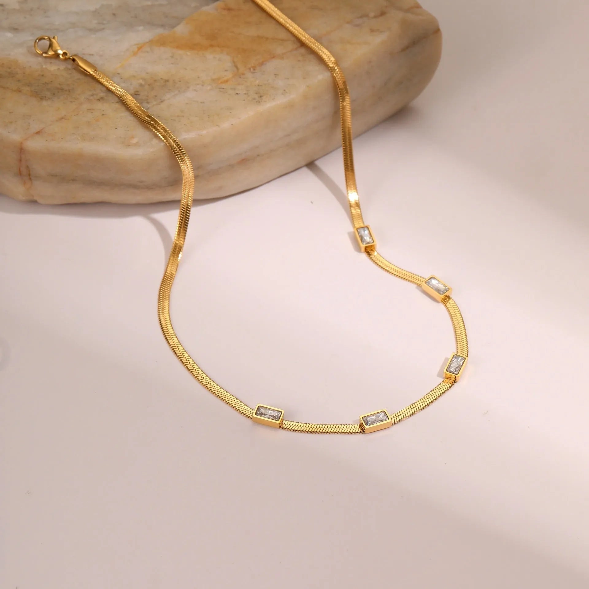 Geometric square zircon pendant on a stainless steel flat snake chain necklace with gold plating.
