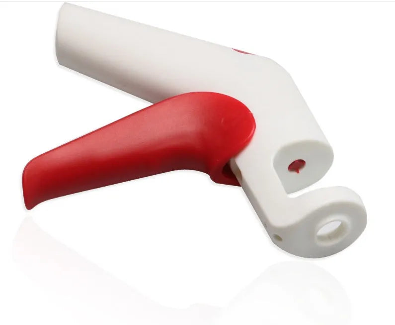 Red and black manual cherry pitter tool with detachable stone catcher on a kitchen worktop.