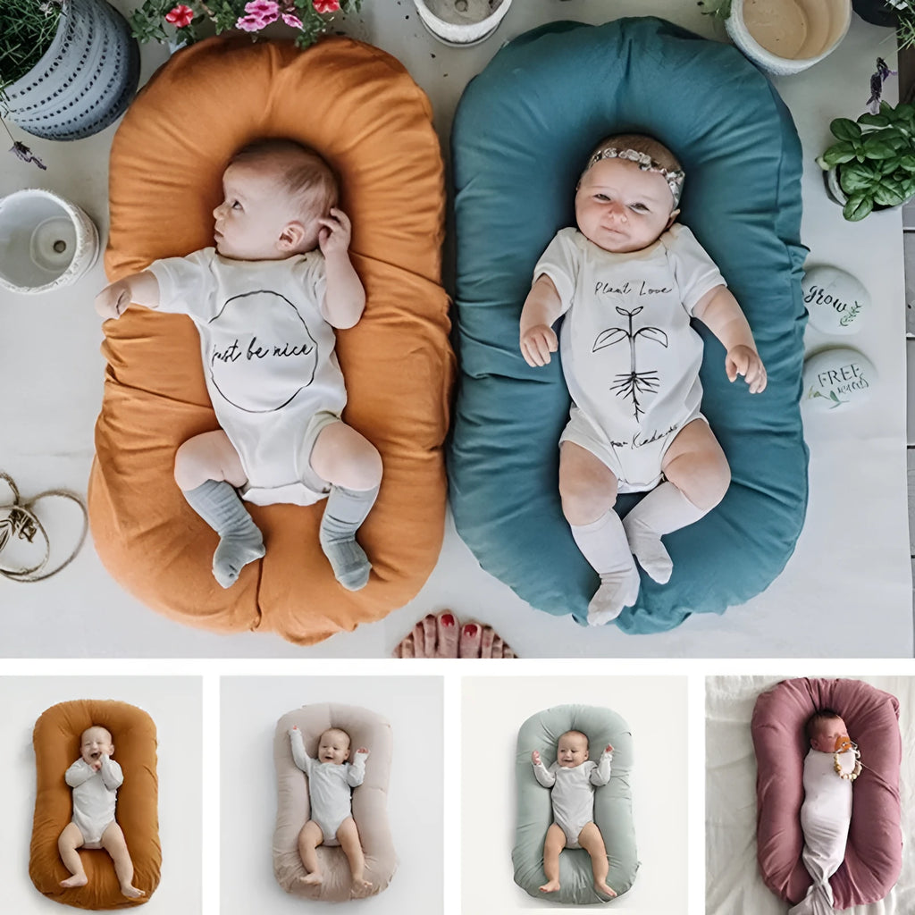 Beige portable baby nest crib cot for newborns on a neutral background.