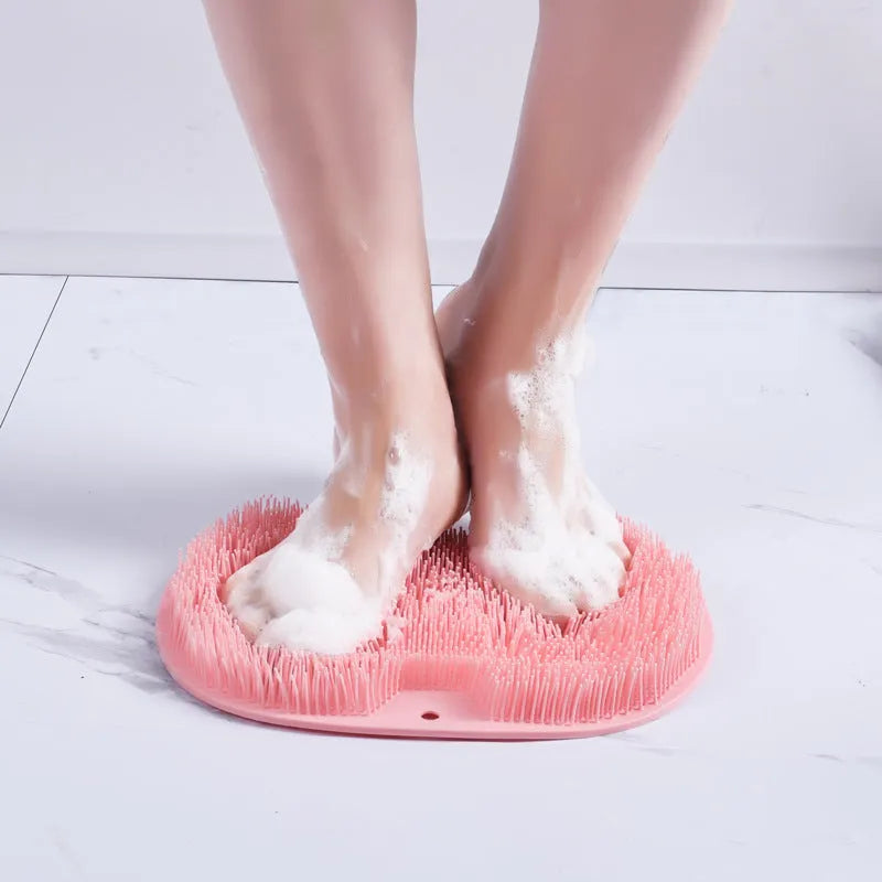 Orange silicone suction cup bath brush mat with bristles for foot and back cleaning on a bathroom floor.