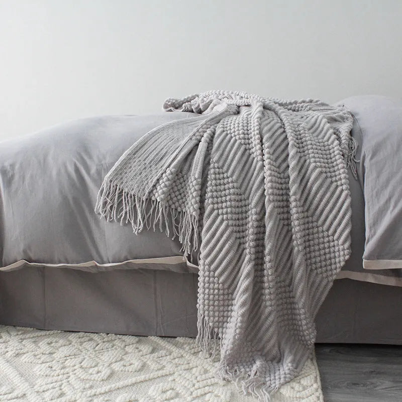 Small polyester fibre throw blanket in dark grey, folded on a sofa