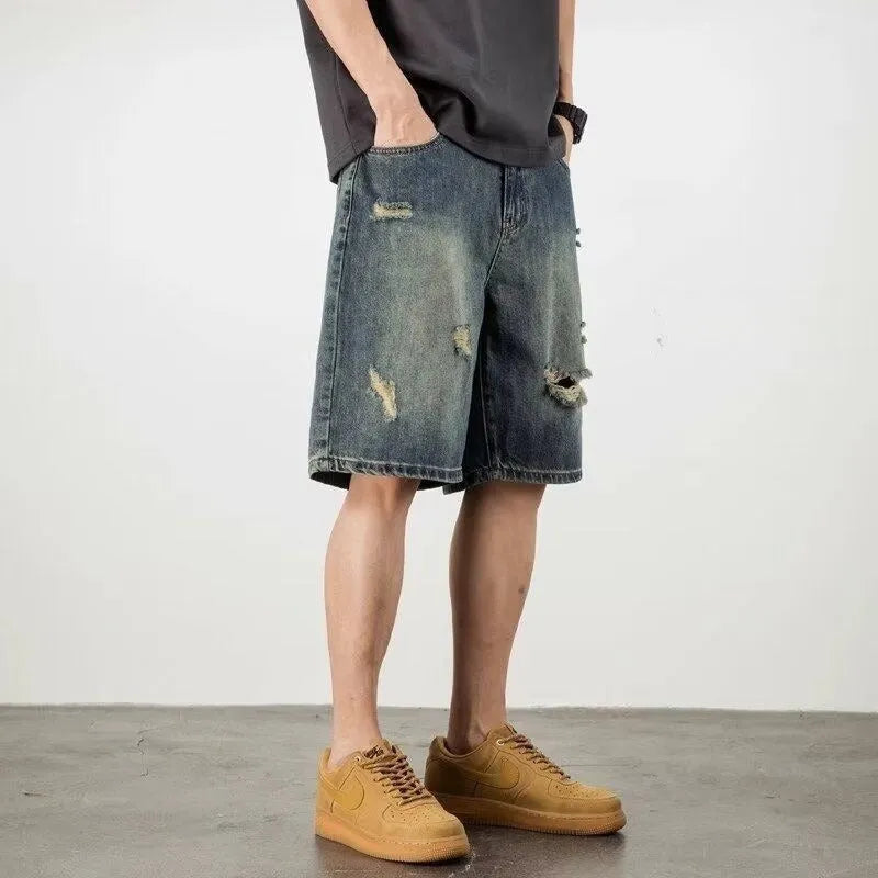Blue men's distressed denim shorts with a loose, straight leg fit on a model.