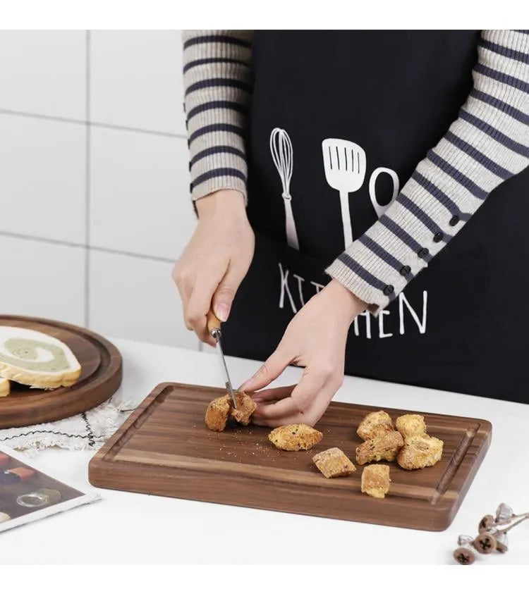 Black walnut wood cutting board with sauce groove and carved side handle on kitchen counter