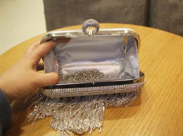Silver ladies fringed hand bag with shiny diamond embellishments and clasp closure on a plain background