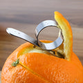Stainless steel ring orange peeler on a countertop with citrus fruits nearby, showing compact silver tool