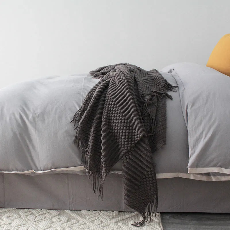 Small polyester fibre throw blanket in dark grey, folded on a sofa
