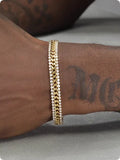 Gold coloured hip hop style tennis bracelet with chain links and artificial gemstone inlays on a wrist.