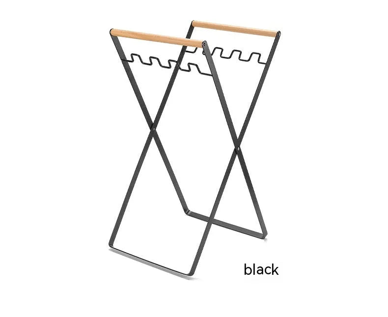 Black iron folding trash rack with wooden handle holding a bin bag outdoors.