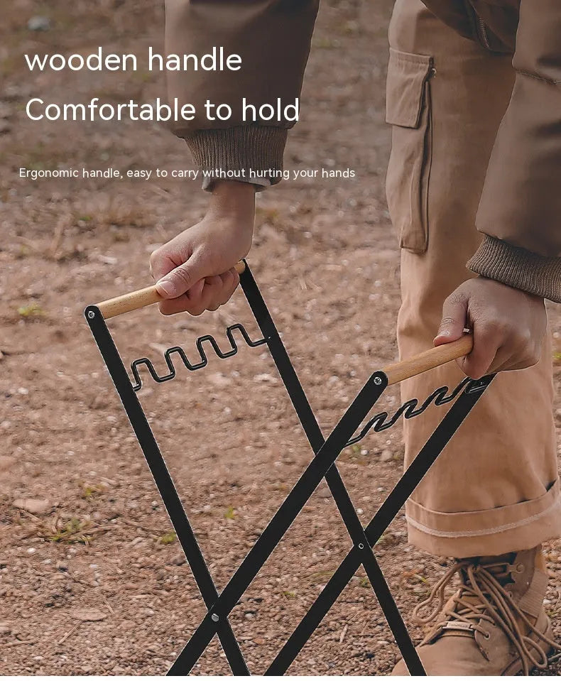 Black iron folding trash rack with wooden handle holding a bin bag outdoors.