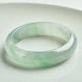 Natural light green jade bracelet with a metal clasp, shown on a wrist.