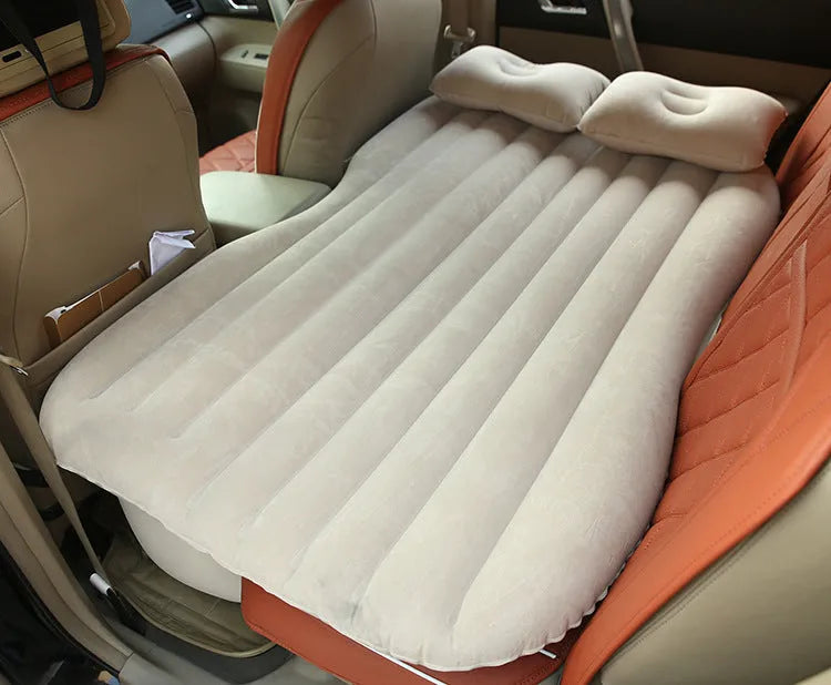 Inflatable car bed with flocked surface folded beside storage bag and two pillows