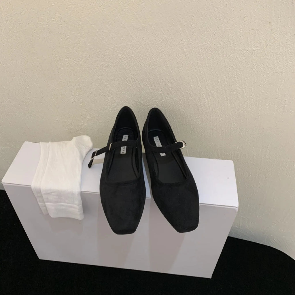 Women's black suede flat shoes with buckle closure and low heel on a neutral background