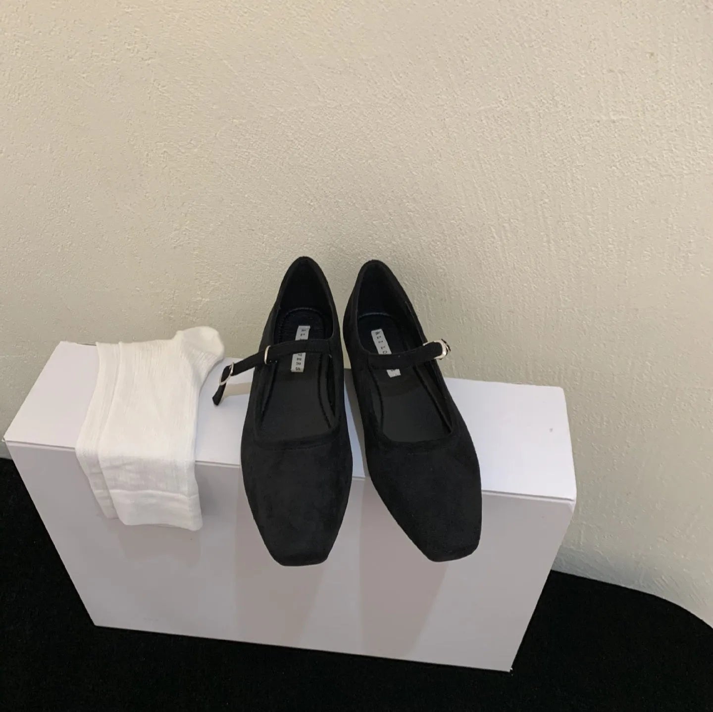 Women's black suede flat shoes with buckle closure and low heel on a neutral background