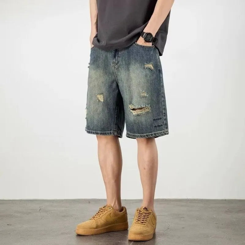 Blue men's distressed denim shorts with a loose, straight leg fit on a model.