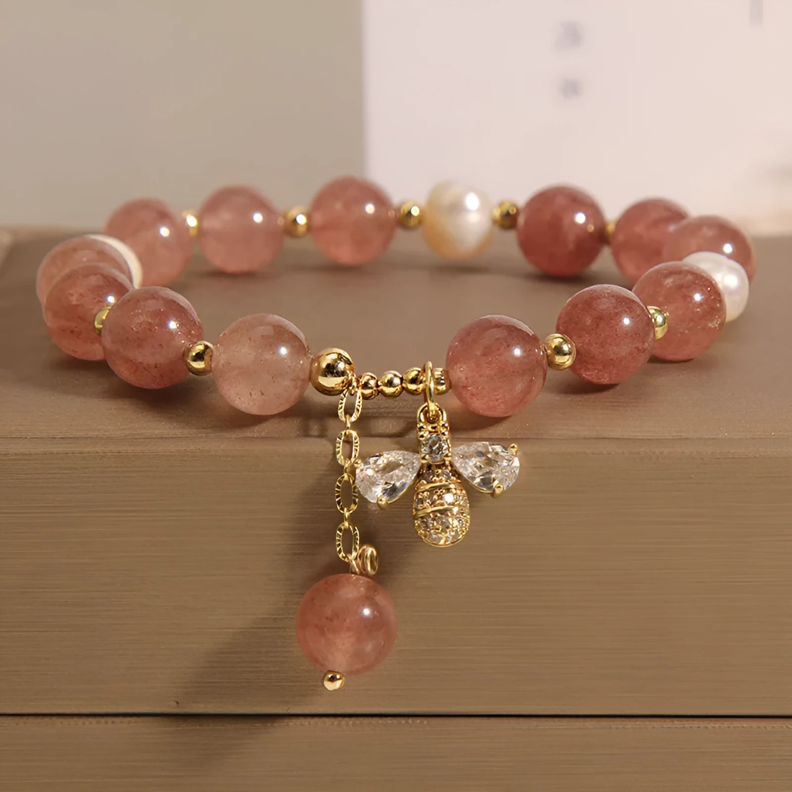 Women's pink strawberry quartz and white freshwater pearl bracelet with zircon details on wrist.