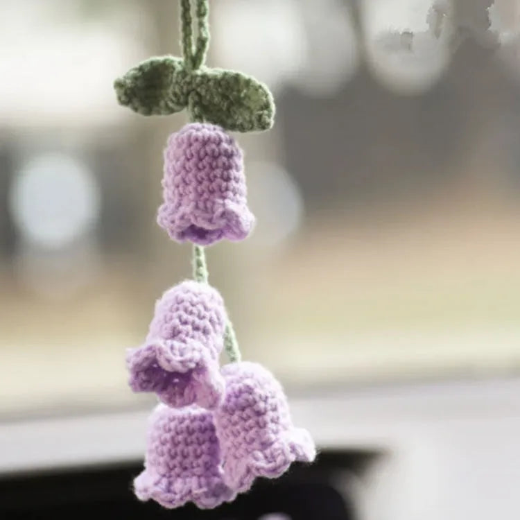 Green and white crocheted car plant decoration with hanging rope on a car dashboard.