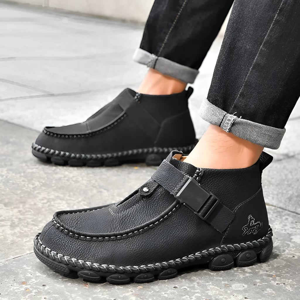 Men's black handmade stitching slip-on loafers with a flat heel on a wooden floor.