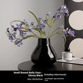 Black ceramic vase with round belly shape and two white flower ornaments arranged decoratively