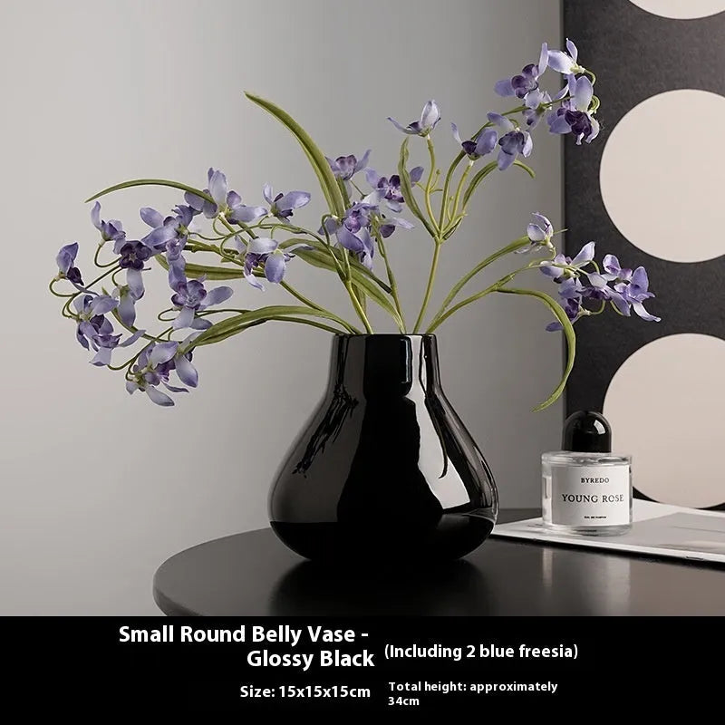 Black ceramic vase with round belly shape and two white flower ornaments arranged decoratively