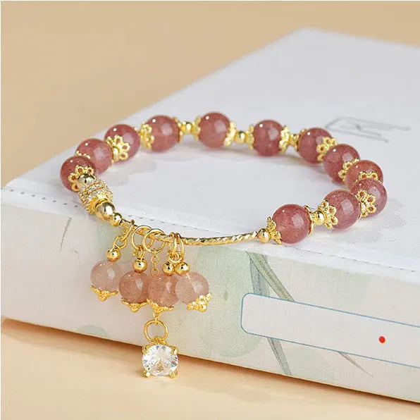 Close-up of a women's pink strawberry quartz heart bracelet with pearl details on a wrist.