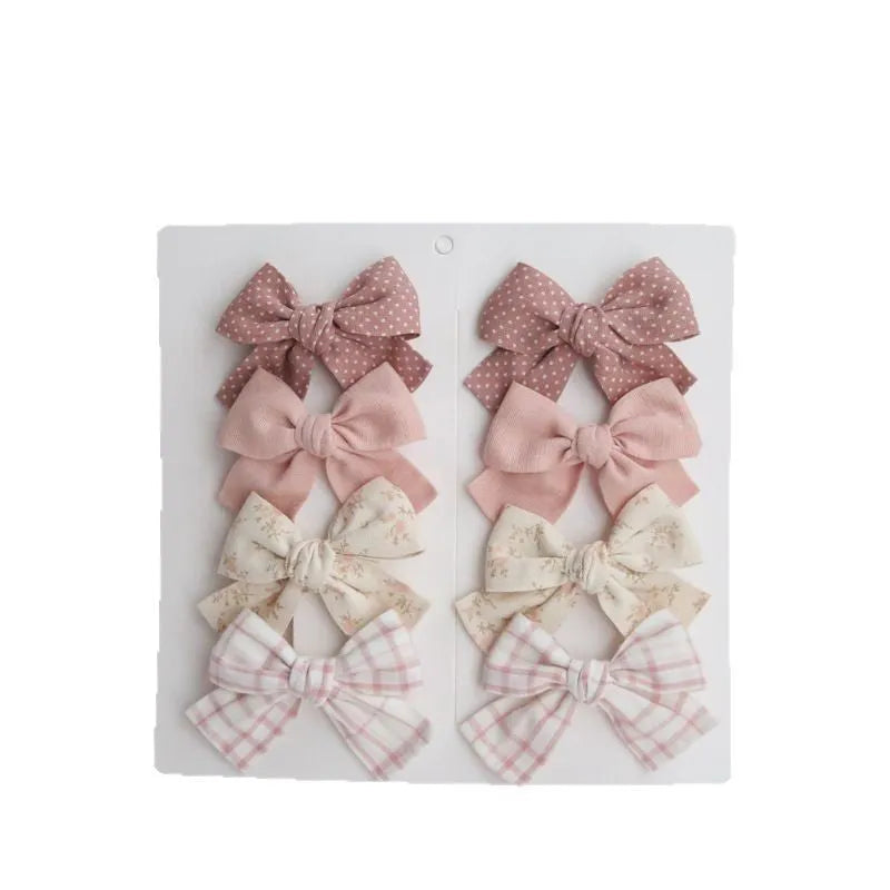 Set of fabric dovetail bow hair clips for children in various colours including beige, pink, and blue flowers.