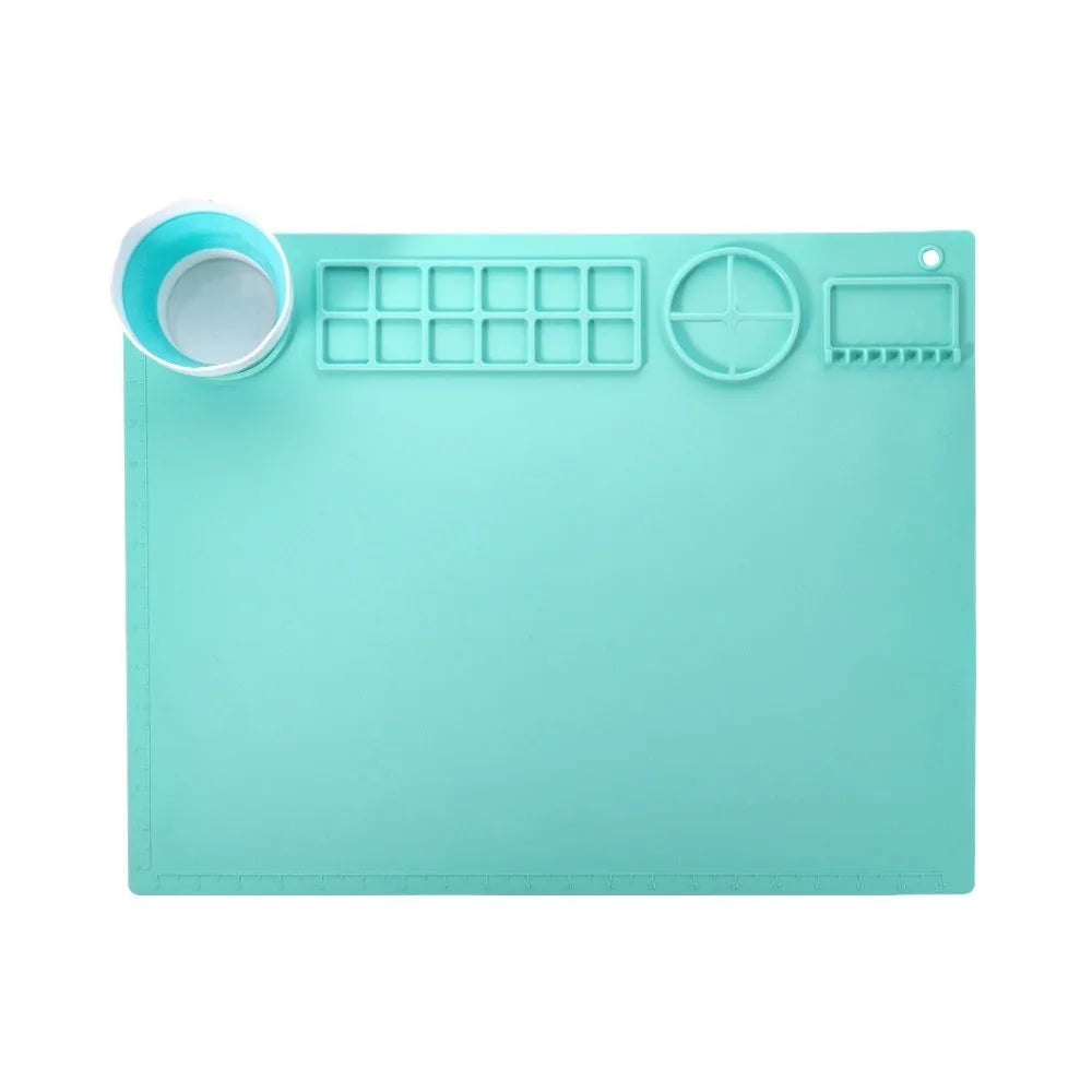 Light blue silicone painting mat with two round mixing bowls, placed on a wooden table with paintbrushes.
