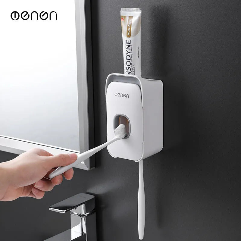 Wall-mounted automatic toothpaste dispenser in blue, grey, or pink colours with a visible dispensing lever.
