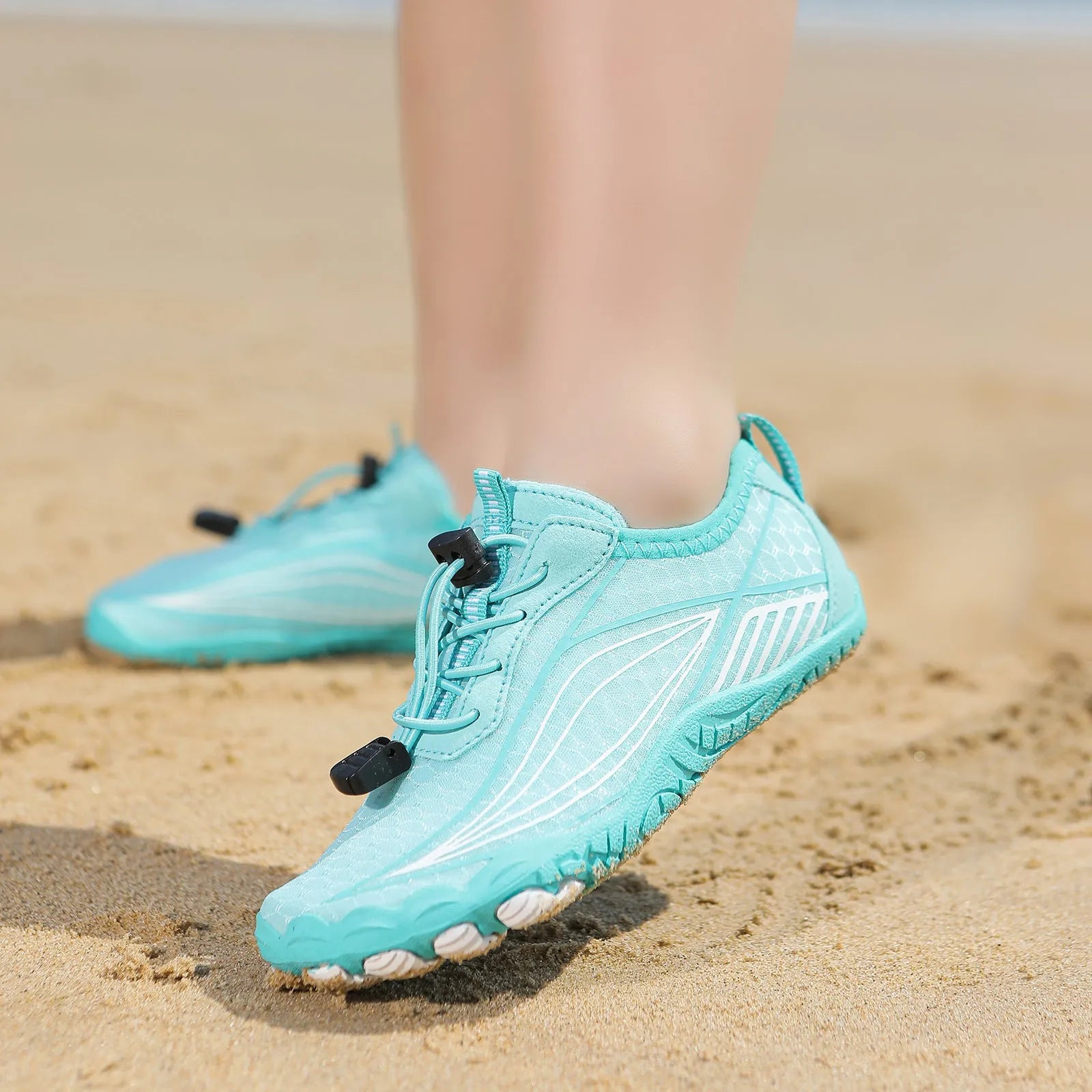 Children's elastic band water shoes in blue with a non-slip rubber sole, shown on a sandy beach.