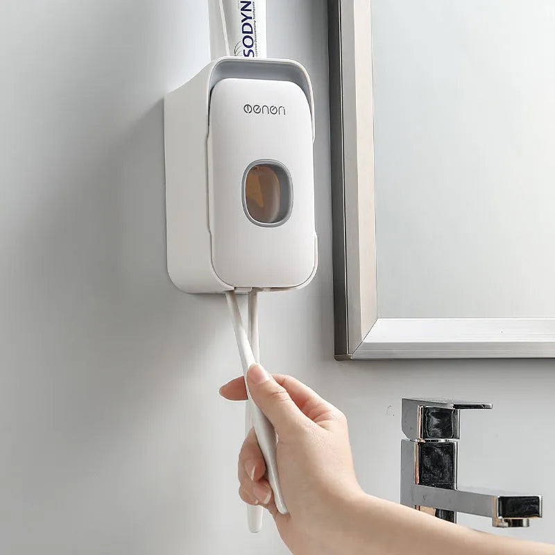 Wall-mounted automatic toothpaste dispenser in blue, grey, or pink colours with a visible dispensing lever.