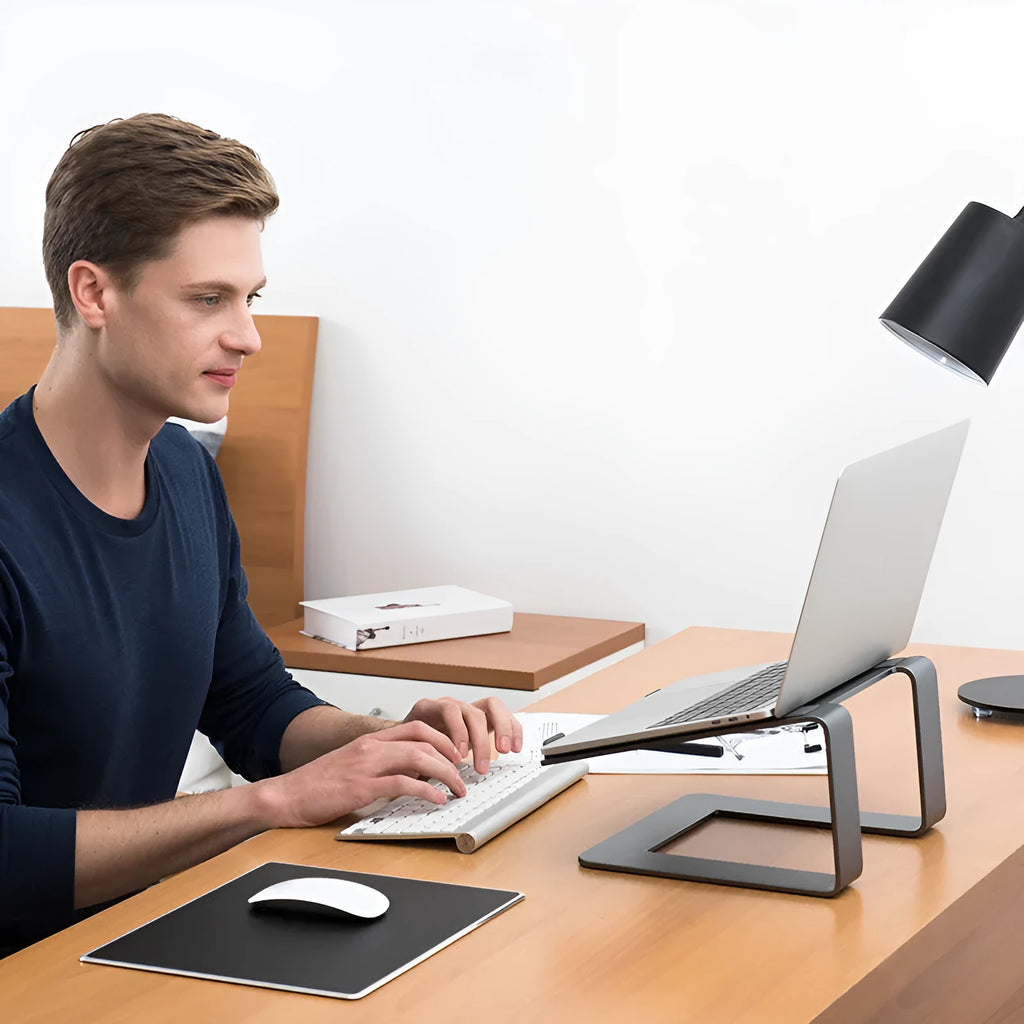 Black aluminium alloy laptop stand on a desk, showing its wide base plate and elevated height.