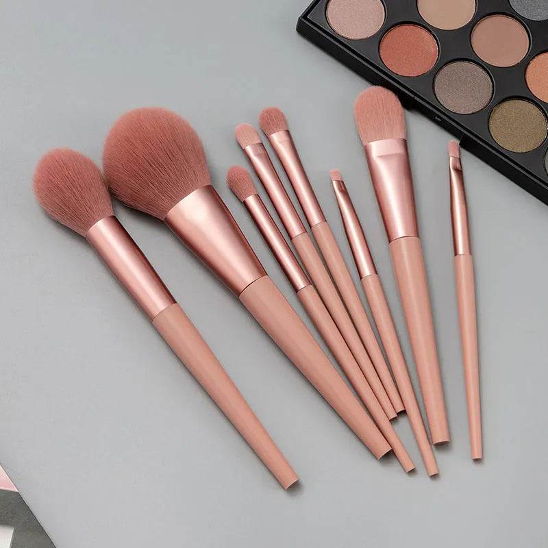 Pink 8-piece makeup brush set with man-made fibre bristles and plastic handles on a light background.