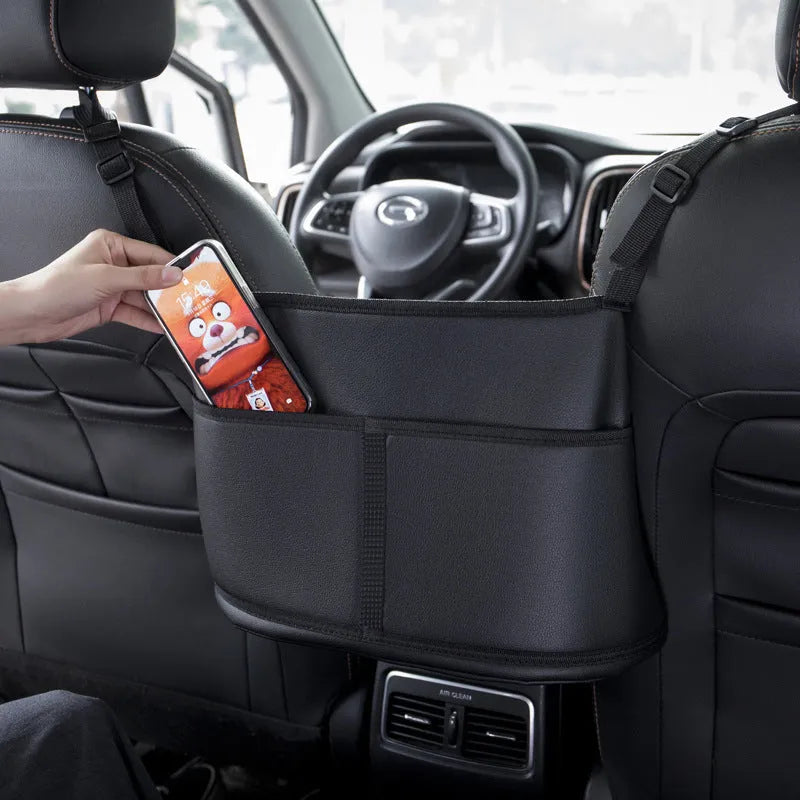Black leather car seat storage bag with carbon fibre pattern, shown between vehicle front seats.