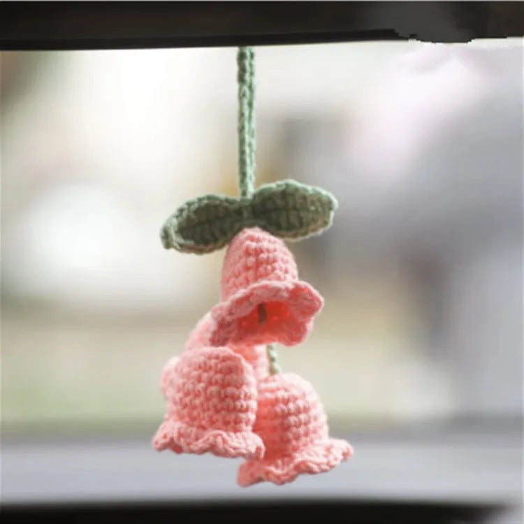 Green and white crocheted car plant decoration with hanging rope on a car dashboard.